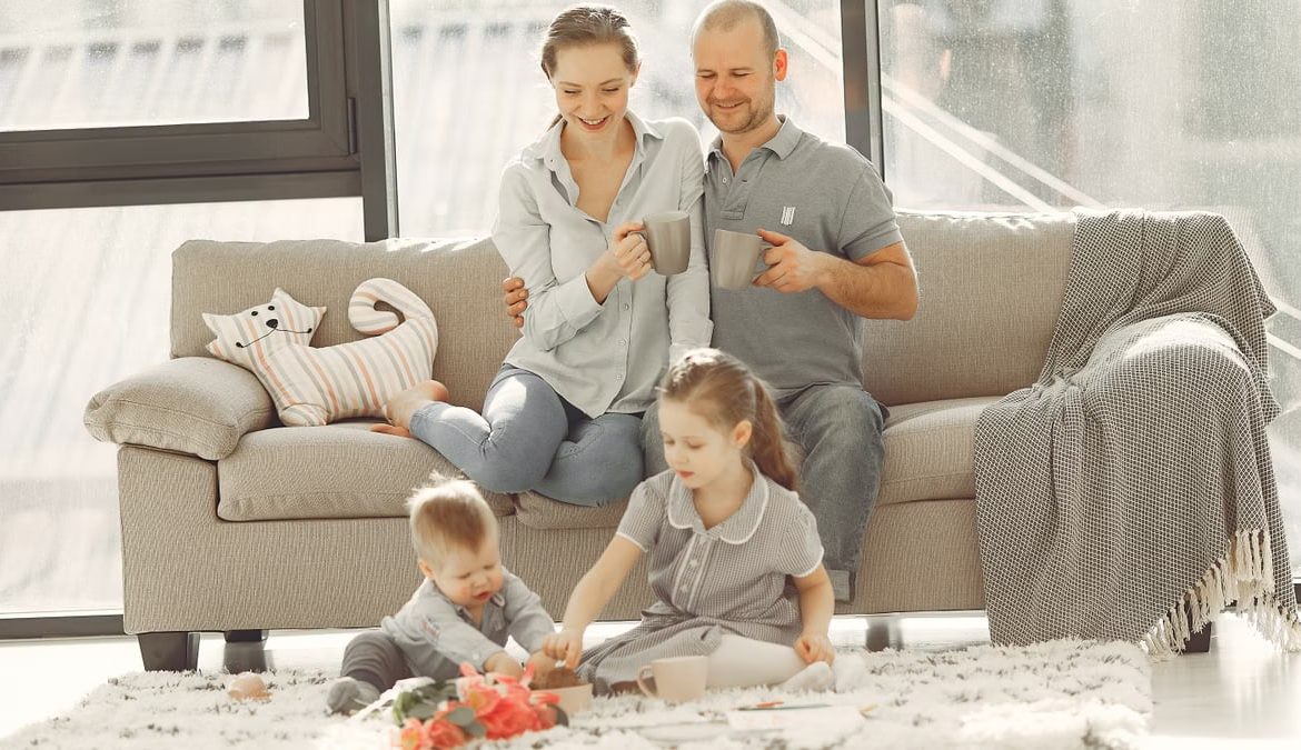 Cheerful family wearing casual clothes sitting in living room while playing and drinking tea during weekend at home in morning